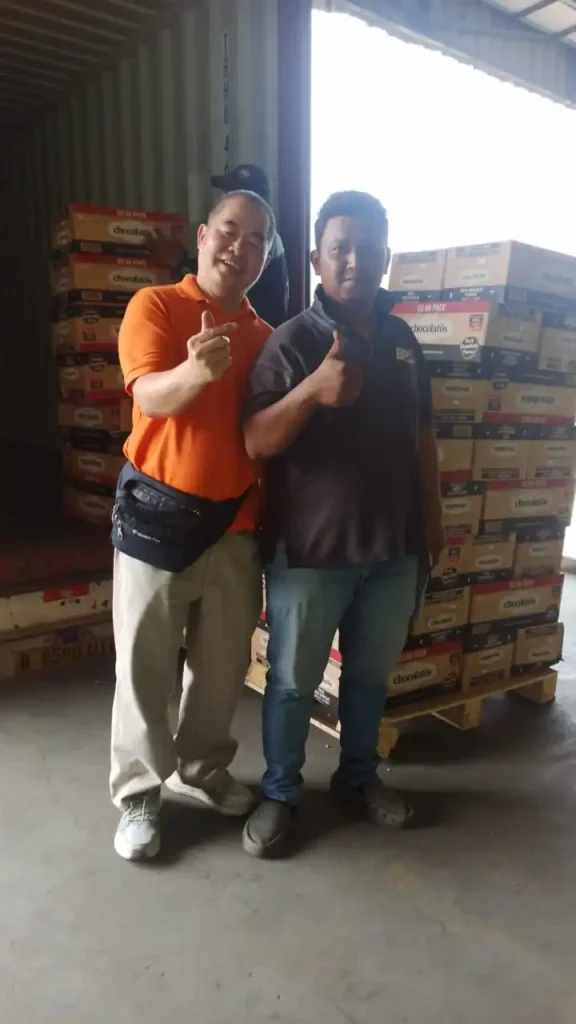 Two workers showing thumbs up at warehouse with chocolatos inventory from Inti Mandiri Jayatama